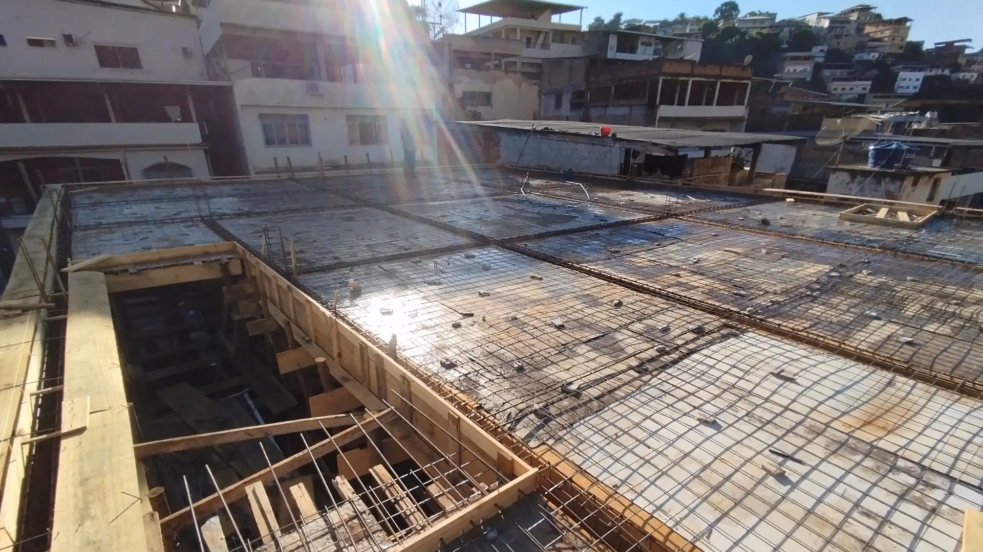 Laje em processo de armação e concretagem com malha de ferro, sob luz solar, mostrando a escala da engenharia